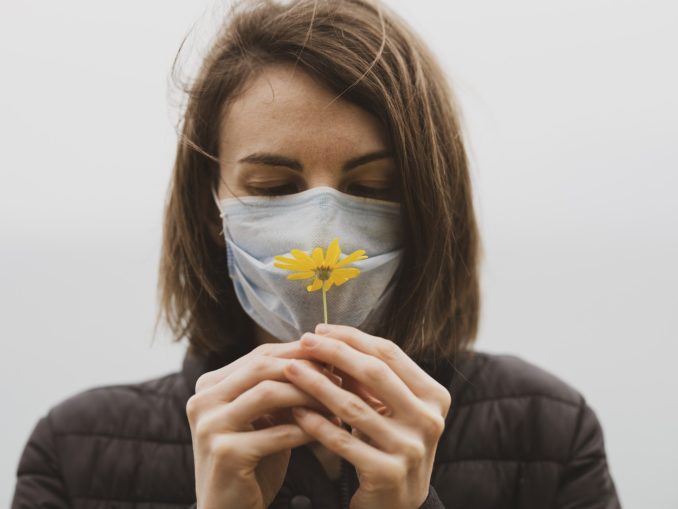 Femme avec masque facial et une fleur à la main