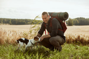 Homme portant un sac à dos de randonnée avec une chien dans un champ